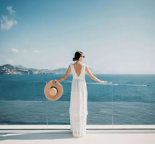 Braut in einem Hochzeitskleid hält einen Hut im 7Pines Resort mit Blick auf das Meer