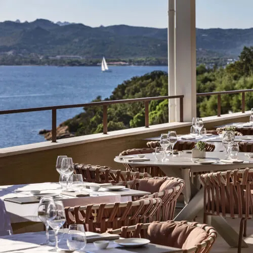 Luxuriose Terrasse des 7Pines Resorts Ibiza mit Tischen am ruhigen Gewaesser