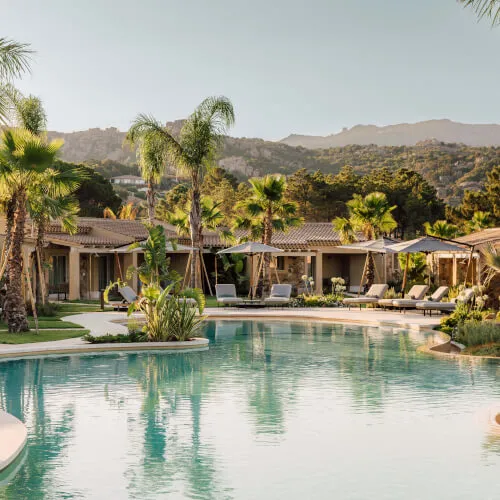 7Pines Resort Sardinien mit einem Pool, Palmen und einem Gebäude, das einen ruhigen Urlaubsort zeigt.