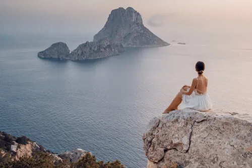 Eine Frau in einem Hochzeitskleid auf einem Felsen am Meer bei 7Pines, die den gelassenen Luxus von Destination by Hyatt verkörpert.